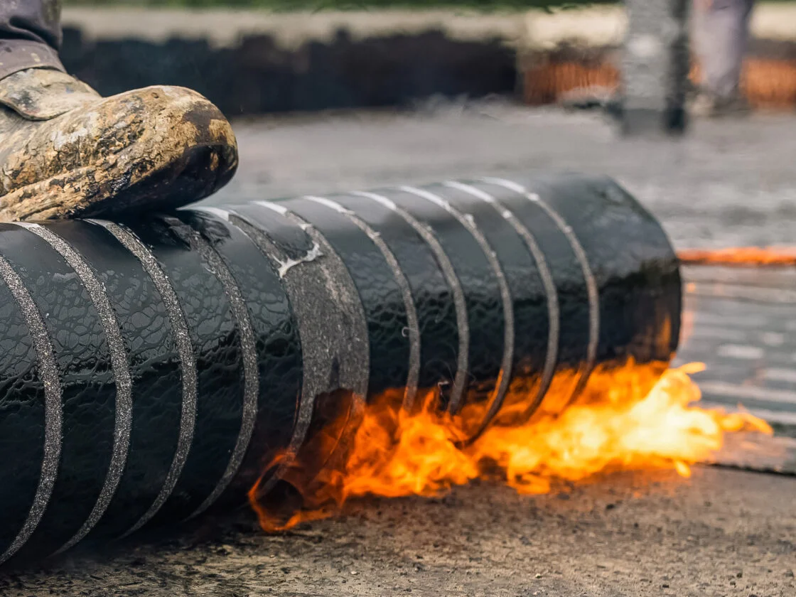 Aufgerollte Bitumen-Schweißbahn wird mit offener Flamme angeschweißt zur Dach- und Gebäudeabdichtung.