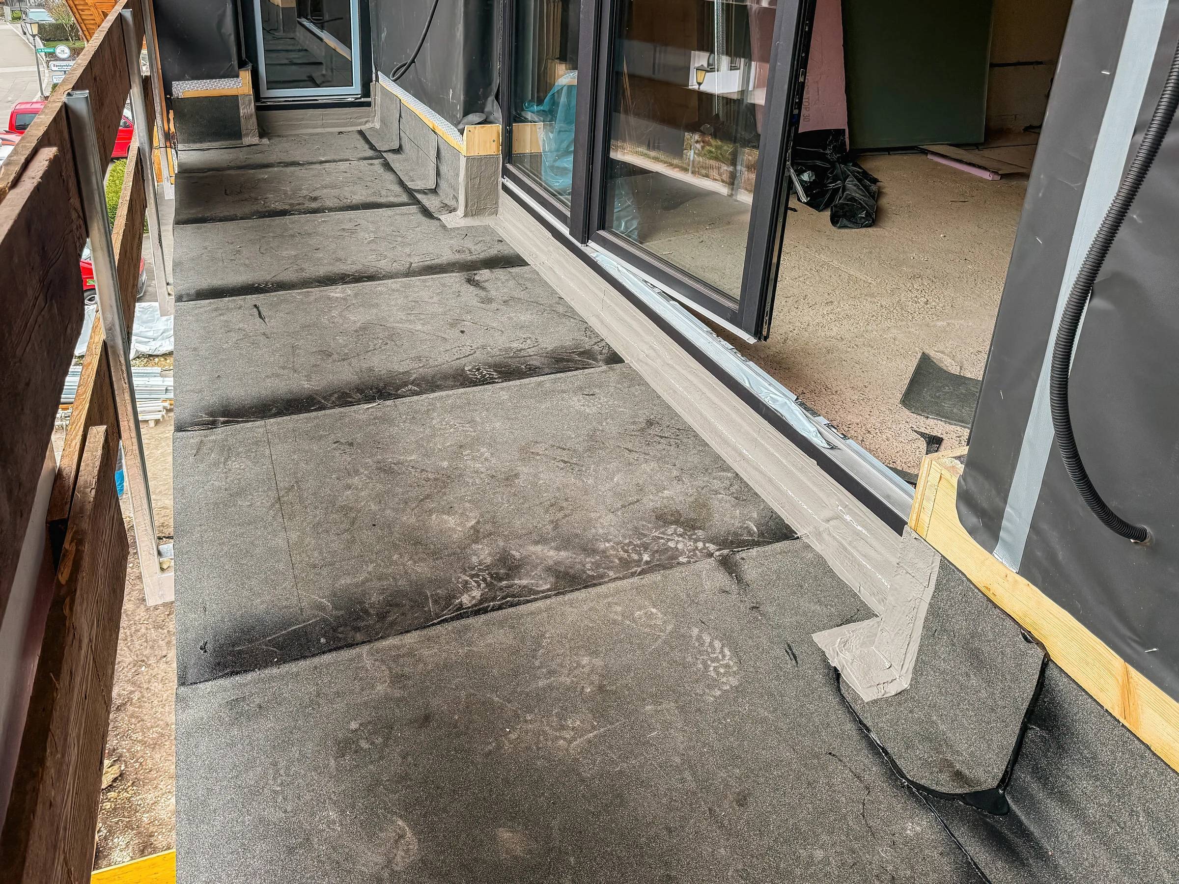 Betonplatten auf Stelzlagern vor Glas-Schiebetür, einige Platten entfernt, Abstandshalter und Werkzeug liegen daneben.