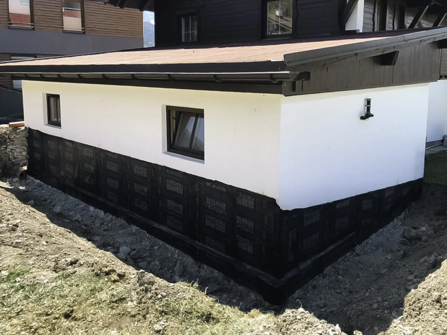 Gebäude mit neu abgedichteter Kelleraußenwand; schwarze Abdichtungsbahn bis Fensterunterkante, weiß verputzte Fassade.