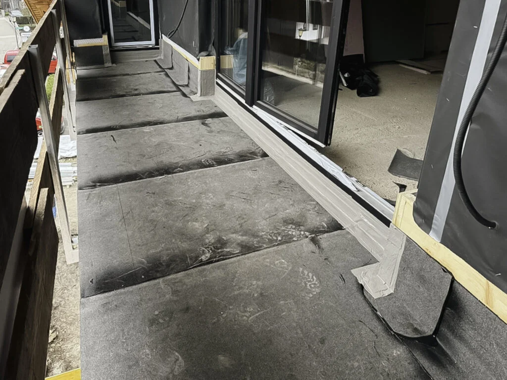 Reihenweise Betonplatten auf Balkon vor bodentiefen Glasschiebetüren, offene Fugen und Klebeband am Rand