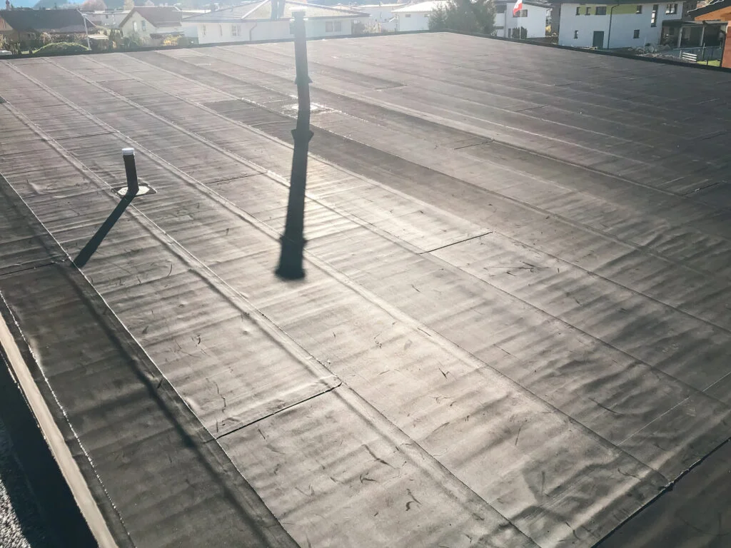 Flachdach mit aufgebrachter Abdichtungsbahn, parallele Nähte, zwei Lüftungsrohre und niedrige Attika