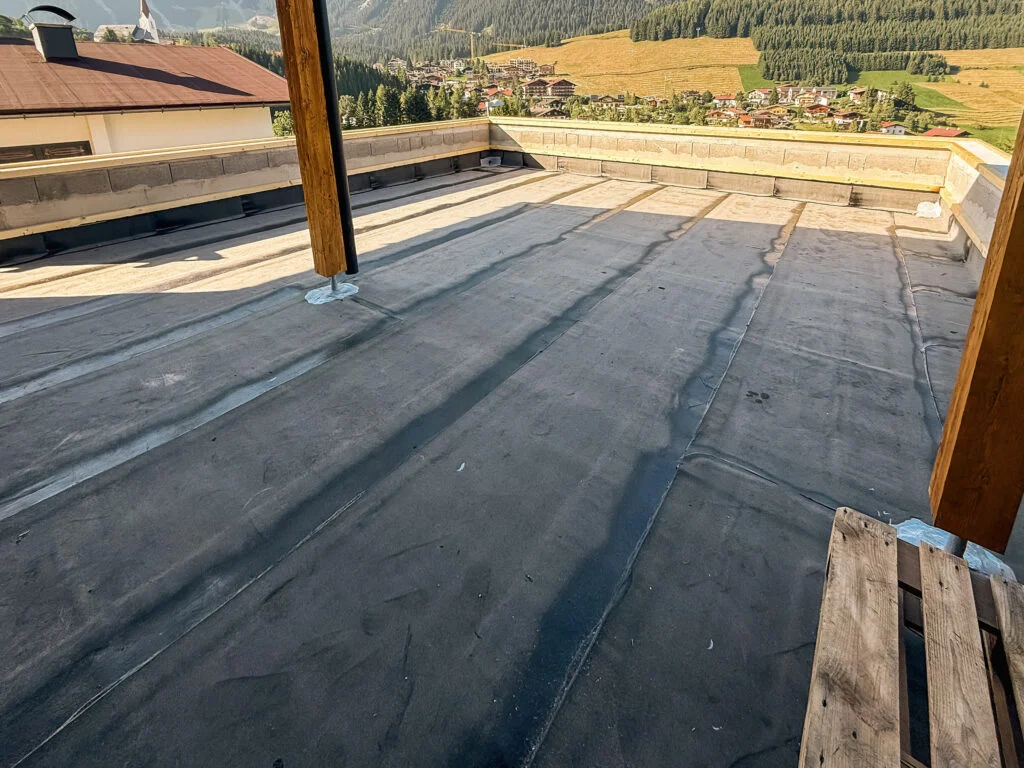 Terrassenabdichtung mit aufgebrachter schwarzer Bitumenbahn, Randanschluss und weiter Blick auf Felder und Berge.