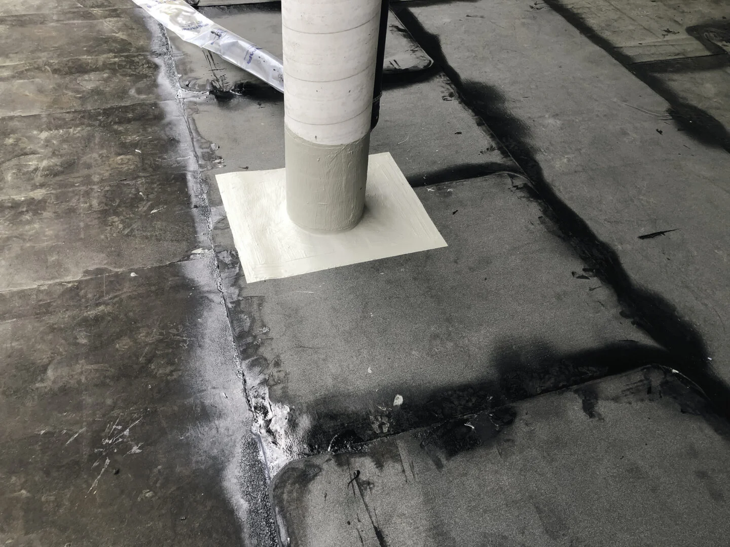 Dach mit schwarzer Flüssigkunststoff-Abdichtung und quadratischer Manschette um Rohrdurchführung