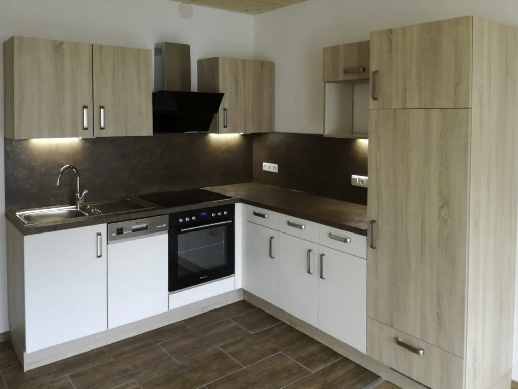 Eckk&uuml;che mit wei&szlig;en Unterschr&auml;nken, Holz-Oberschr&auml;nken, Dunstabzug, Herd/Backofen und Arbeitsplatte.