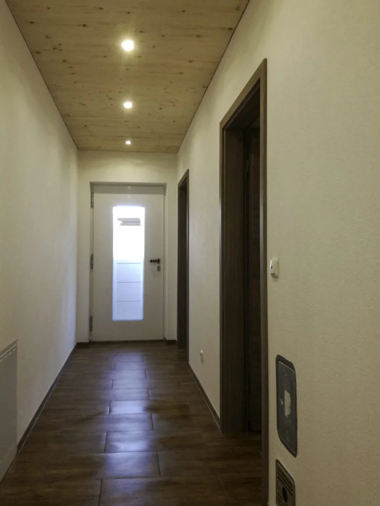 Schmaler Wohnungsflur mit hellen W&auml;nden, braunen Bodenfliesen, drei Decken-Einbaustrahlern und Innent&uuml;r mit satiniertem Glas.