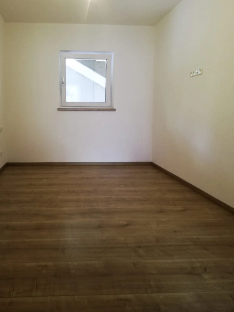 Leeres Zimmer in Mietwohnung, wei&szlig;e W&auml;nde, dunkles Laminat, kleines rechteckiges Fenster