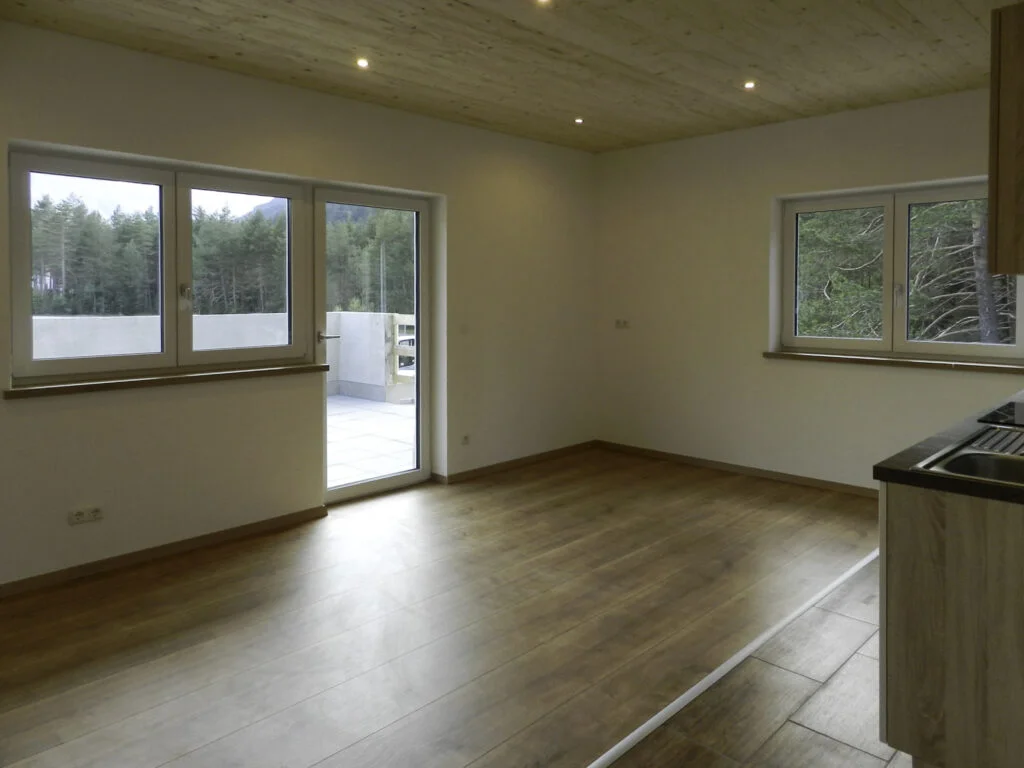 Leerer Wohnraum in Mietwohnung: helles Laminat, wei&szlig;e W&auml;nde, Decken-Einbauspots, gro&szlig;e Terrassent&uuml;r, Fenster, Heizk&ouml;rper.