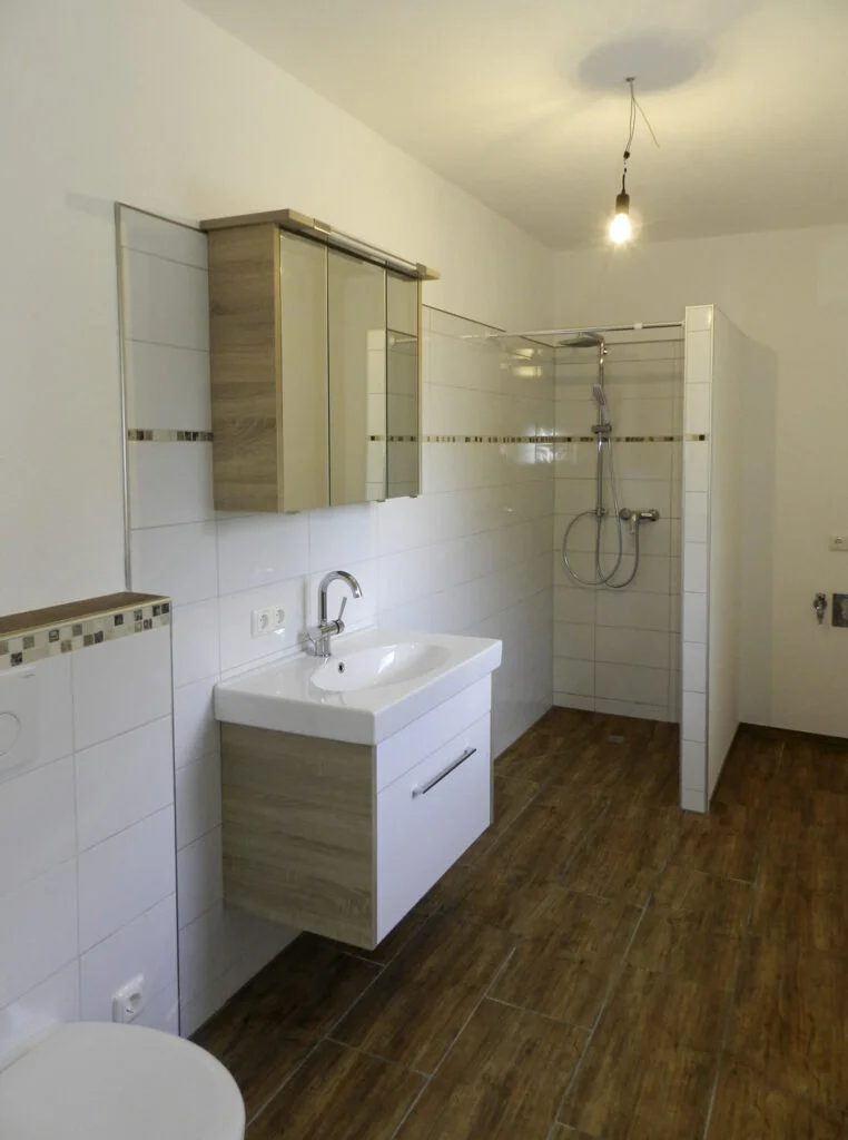 Badezimmer in Mietwohnung: Waschbecken mit Unterschrank und Spiegelschrank, offene Duschnische, Handtuchheizk&ouml;rper.