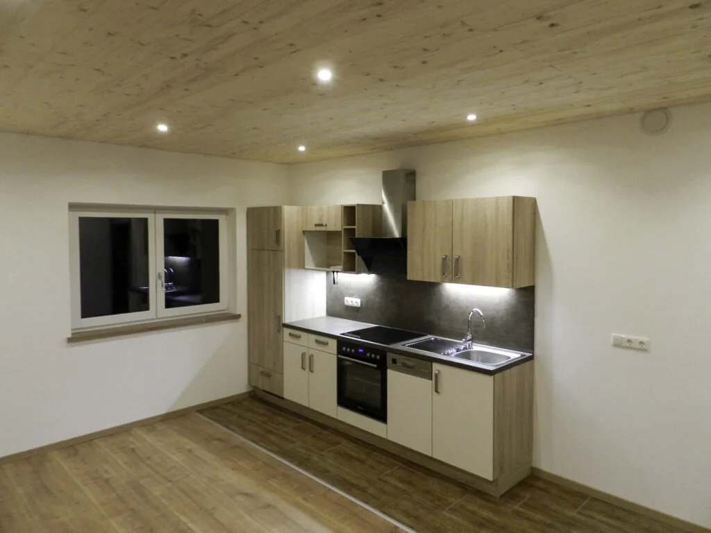 Kleine Einbauk&uuml;che in Mietwohnung mit Backofen, Kochfeld, Sp&uuml;le, Oberschr&auml;nken, Fenster, Heizk&ouml;rper und Holzdecke