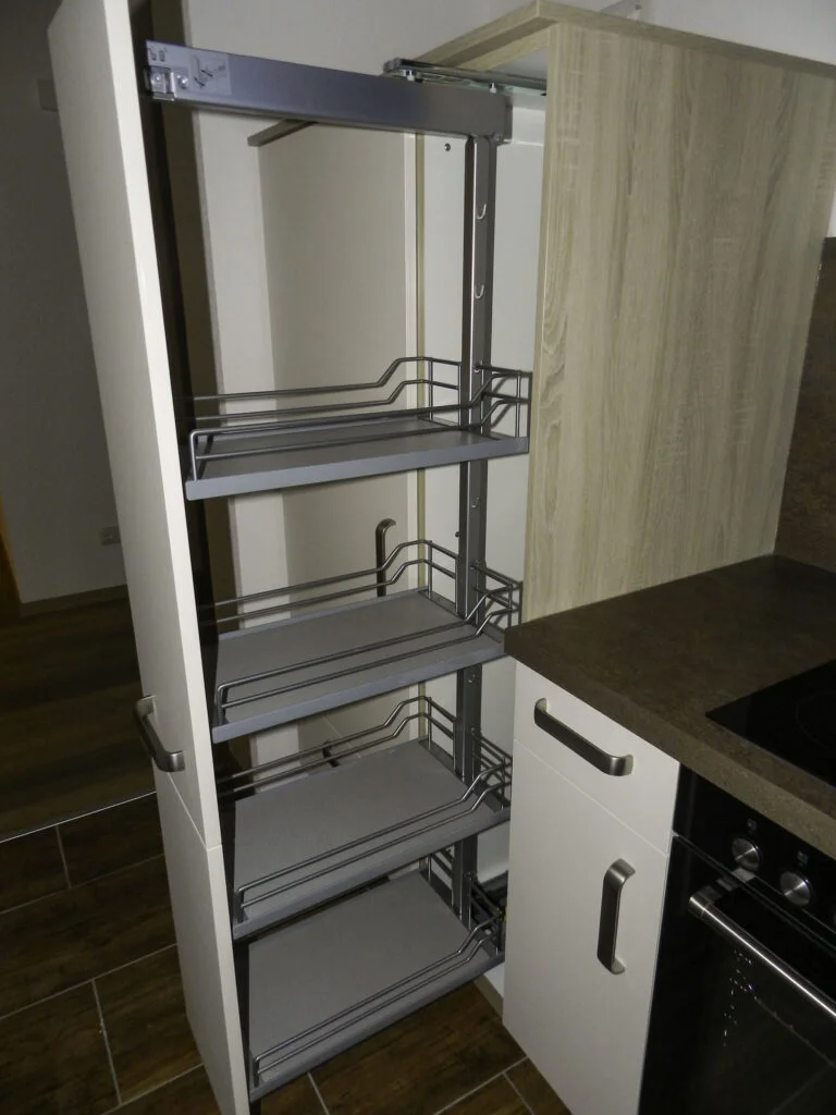 Schmaler Auszugsschrank mit drei Metallk&ouml;rben neben Einbauherd und Hochschrank in K&uuml;chenzeile.