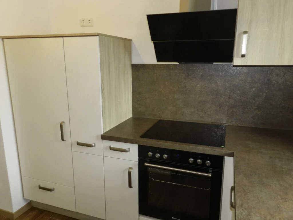 K&uuml;chenzeile mit Elektroherd und Backofen, schwarzer Dunstabzug, grauer R&uuml;ckwand und wei&szlig;en Hochschr&auml;nken