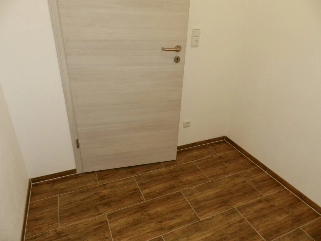Geschlossene helle Zimmert&uuml;r in Ecke mit wei&szlig;en W&auml;nden, braunem Holzfliesenboden, Sockelleiste und Steckdose