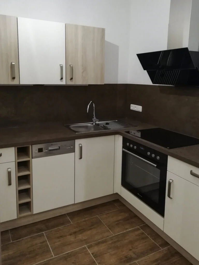 K&uuml;chenzeile in Mietwohnung: wei&szlig;e Schr&auml;nke, schwarze Haube, Sp&uuml;le, Herd, offenes Flaschenfach.