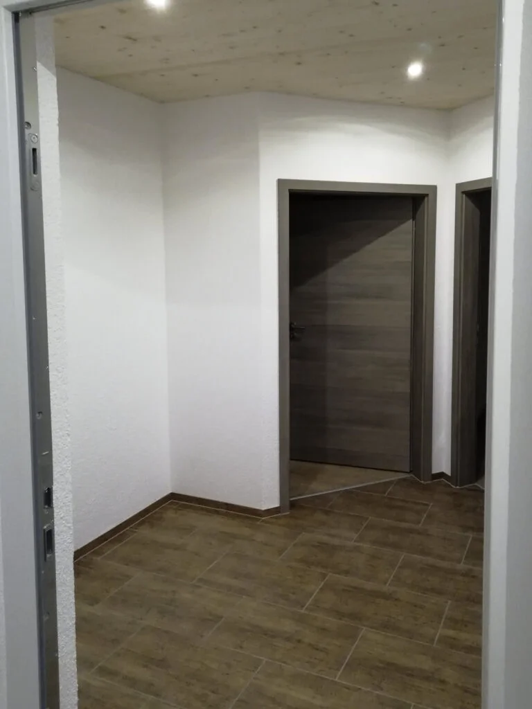 Eingangsbereich eines Wohnungsflurs in einer Mietwohnanlage mit wei&szlig;en W&auml;nden, dunkelbraunem Boden und geschlossener dunkler 