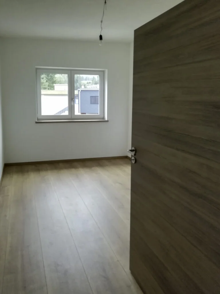 Leeres, helles Zimmer in Mietwohnung; heller Laminatboden, wei&szlig;e W&auml;nde, Fenster mit Heizk&ouml;rper, ge&ouml;ffnete Holzinnent&uuml;r.