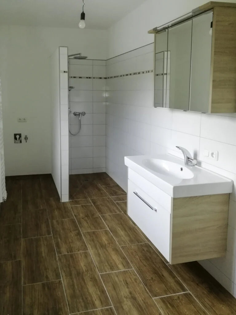 Badezimmer einer Mietwohnung: h&auml;ngender Waschtisch mit Einhebelmischer, offener Duschbereich mit Glas, Holzoptik-Fliesen