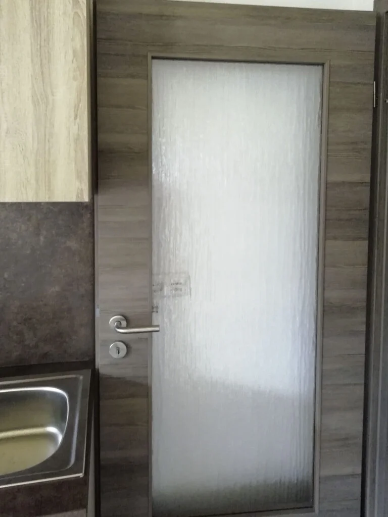 Wohnungsinnent&uuml;r mit mattierter Glasf&uuml;llung und silbernem T&uuml;rgriff; links Sp&uuml;le und Arbeitsplatte, Holzrahmen